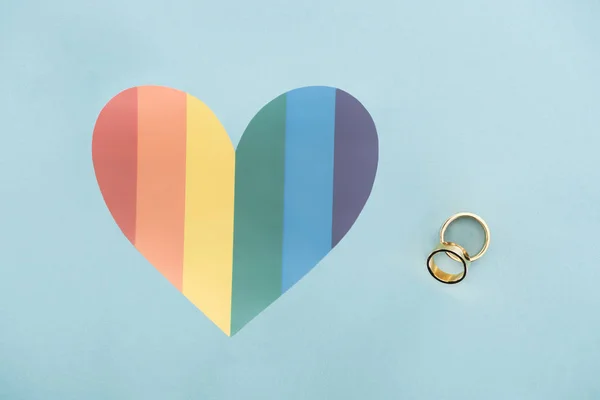 Anillos de boda sobre fondo azul con corazón de color arco iris, concepto lgbt - foto de stock