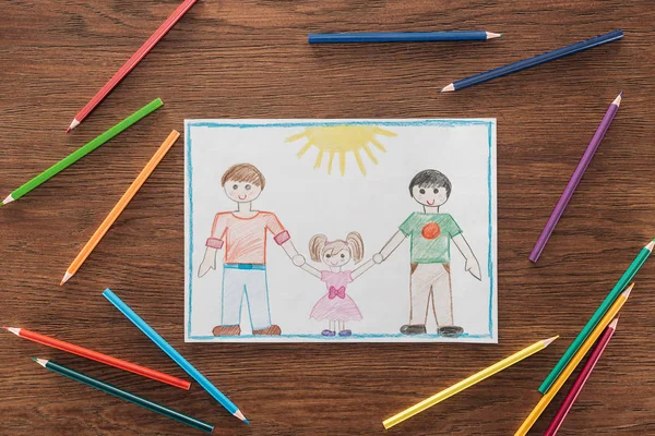 White paper with drawing of same sex family and multicolored pencils on wooden brown surface, lgbt concept — Stock Photo