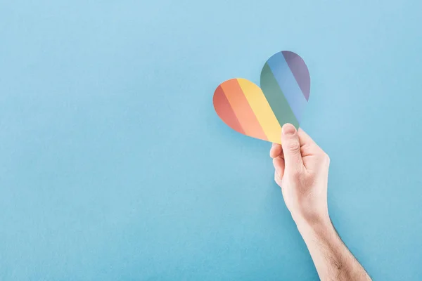 Vue recadrée de la main masculine avec coeur en papier de couleur arc-en-ciel sur fond bleu, concept lgbt — Photo de stock