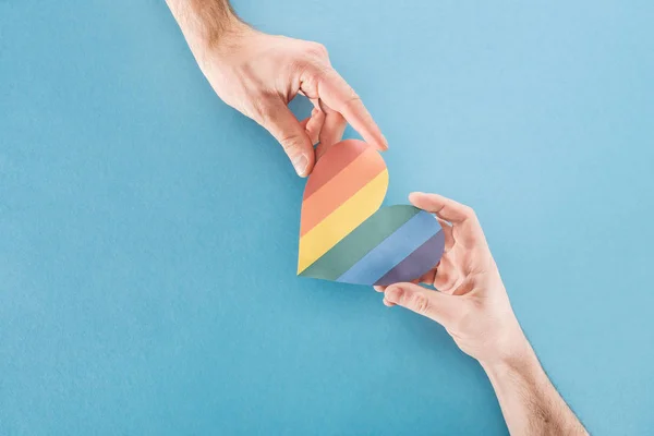 Abgeschnittene Ansicht von Männern mit regenbogenfarbenem Papierherz auf blauem Hintergrund, lgbt concept — Stockfoto