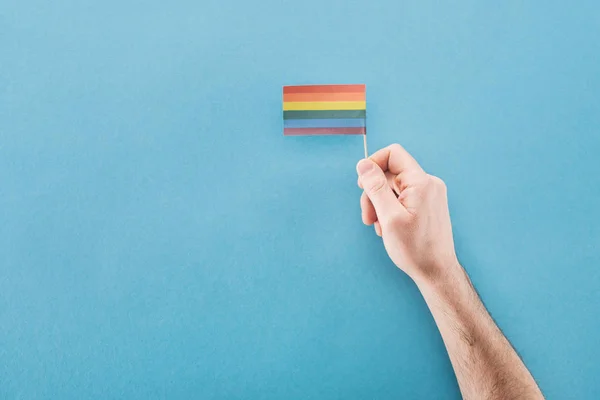 Vista recortada del hombre sosteniendo la bandera del arco iris de papel sobre fondo azul, concepto lgbt - foto de stock