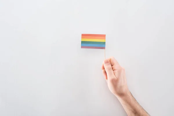 Visão parcial da mão masculina com bandeira do arco-íris de papel no fundo cinza, conceito lgbt — Fotografia de Stock