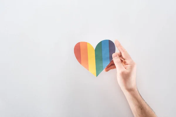 Обрізаний вид чоловічої руки з веселковим кольоровим паперовим серцем на сірому фоні, концепція lgbt — стокове фото