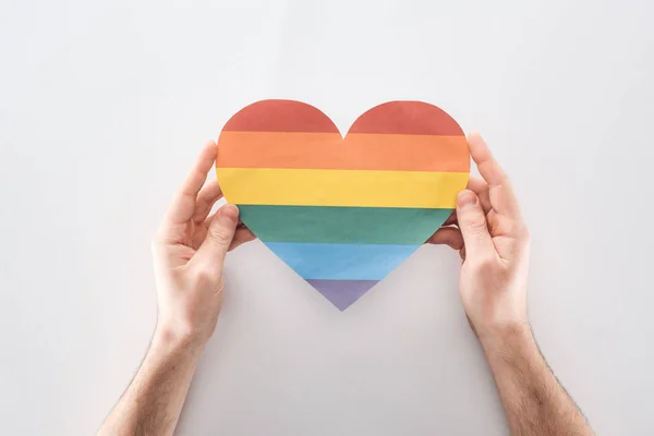 Partial view of man holding paper rainbow colored paper heart on grey background, lgbt concept — Stock Photo