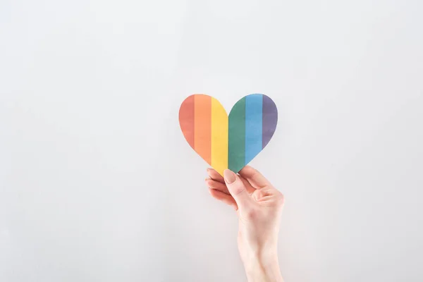 Partial view of female hand with rainbow colored paper heart on grey background, lgbt concept — Stock Photo