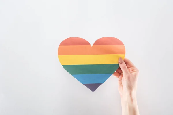 Corte da mão feminina com coração de papel colorido arco-íris isolado no conceito cinza, lgbt — Fotografia de Stock
