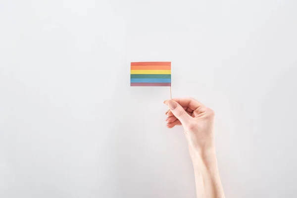Vista parcial de la mano femenina con bandera de arco iris de papel sobre fondo gris, concepto lgbt - foto de stock