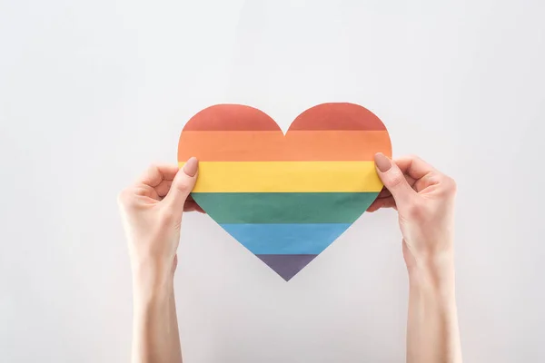Corte de mãos femininas com coração de papel colorido arco-íris isolado em cinza, conceito lgbt — Fotografia de Stock