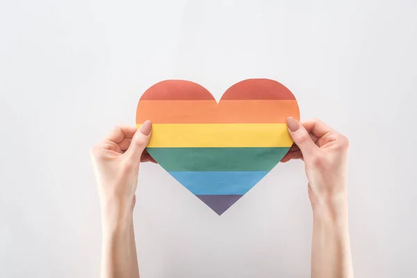 Vue recadrée des mains féminines avec coeur en papier de couleur arc-en-ciel isolé sur gris, concept lgbt — Photo de stock