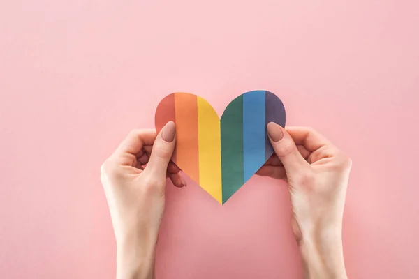 Vista recortada de la mujer sosteniendo el corazón de papel de color arco iris sobre fondo rosa, concepto lgbt - foto de stock