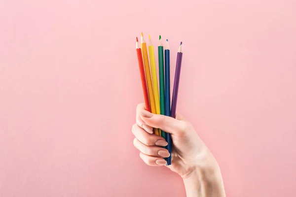 Частковий вигляд жіночої руки з веселковими кольоровими олівцями на рожевому фоні, концепція lgbt — стокове фото