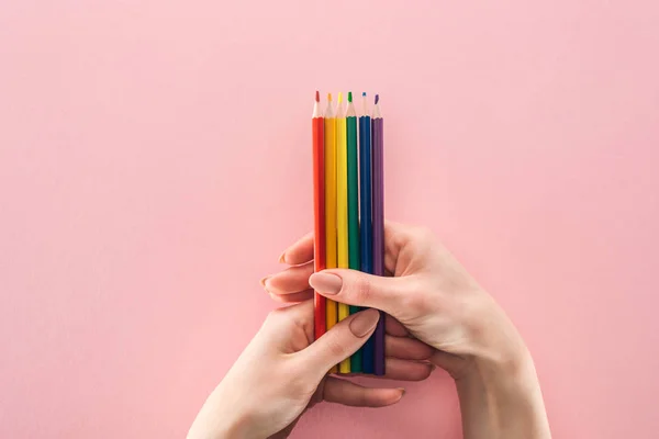 Vista parcial de las manos femeninas con lápices de colores arco iris sobre fondo rosa, concepto lgbt - foto de stock