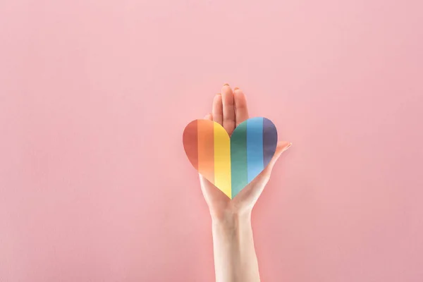 Vista recortada de la mujer sosteniendo el corazón de papel de color arco iris sobre fondo rosa, concepto lgbt - foto de stock