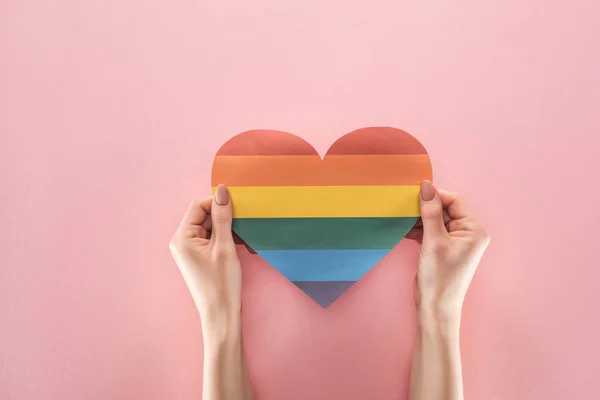 Partial view of woman holding rainbow colored paper heart on pink background, lgbt concept — Stock Photo