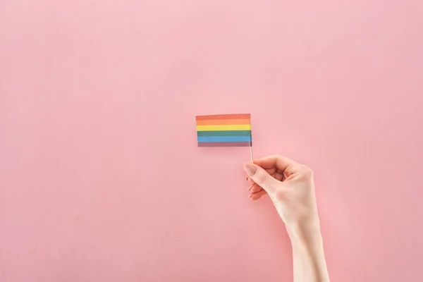 Vue partielle de la main féminine avec drapeau arc-en-ciel en papier sur fond rose, concept lgbt — Photo de stock