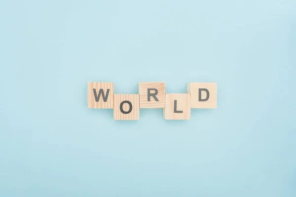 Vista superior de las letras del mundo hechas de cubos de madera sobre fondo azul - foto de stock