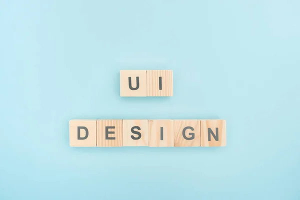 Top view of ui design lettering made of wooden cubes on blue background — Stock Photo