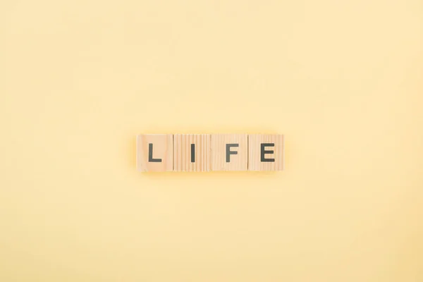 Vista superior de letras de vida hechas de cubos de madera sobre fondo amarillo - foto de stock