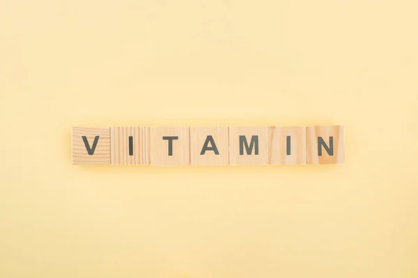 Top view of vitamin lettering made of wooden cubes on yellow background — Stock Photo