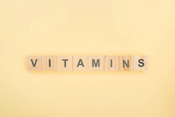 Top view of vitamins lettering made of wooden cubes on yellow background — Stock Photo