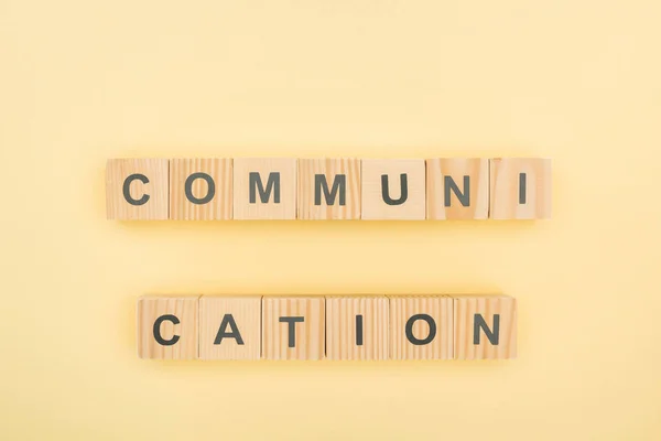 Vue du dessus du lettrage de communication en cubes de bois sur fond jaune — Photo de stock