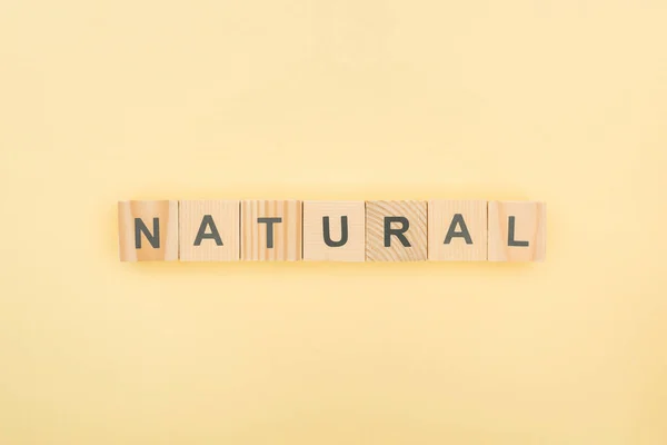 Vue de dessus du lettrage naturel en cubes de bois sur fond jaune — Photo de stock