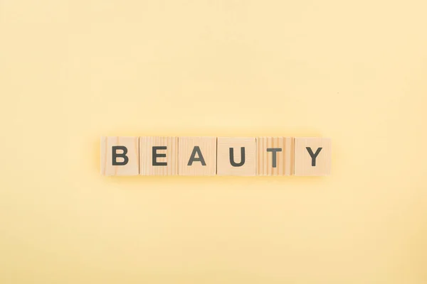 Top view of beauty lettering made of wooden cubes on yellow background — Stock Photo