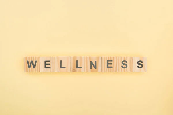 Top view of wellness lettering made of wooden cubes on yellow background — Stock Photo