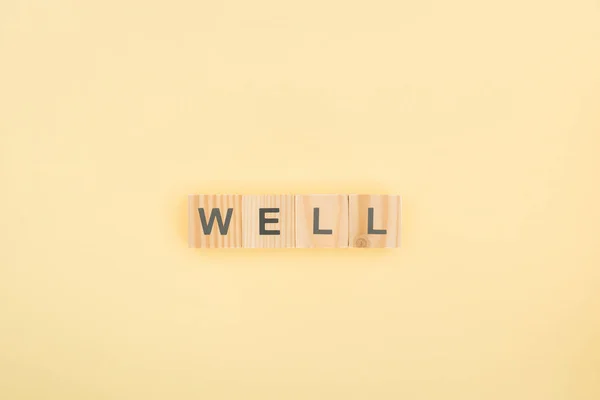 Top view of well lettering made of wooden cubes on yellow background — Stock Photo