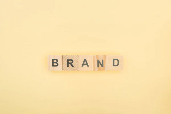 Top view of brand lettering made of wooden cubes on yellow background — Stock Photo