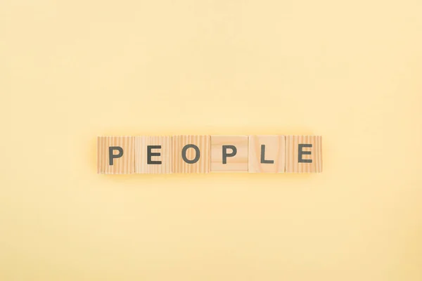 Top view of people lettering made of wooden cubes on yellow background — Stock Photo