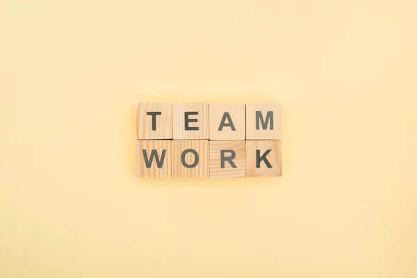 Vista dall'alto del lavoro di squadra lettering fatta di blocchi di legno su sfondo giallo — Foto stock