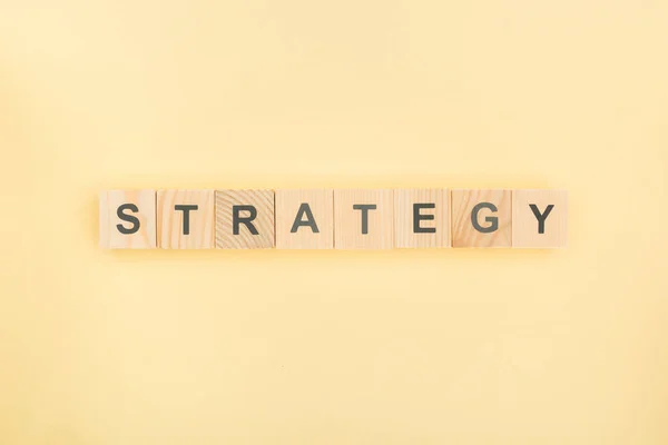 Top view of strategy lettering made of wooden cubes on yellow background — Stock Photo