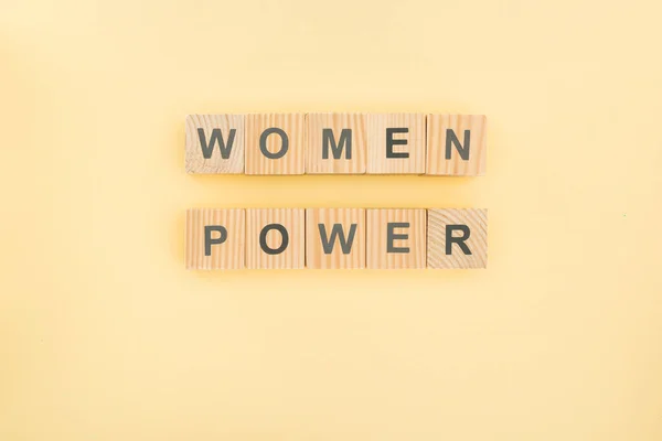 Top view of women power lettering made of wooden cubes on yellow background — стоковое фото