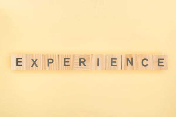 Top view of experience lettering made of wooden cubes on yellow background — Stock Photo