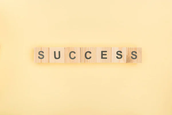 Top view of success lettering made of wooden cubes on yellow background — Stock Photo