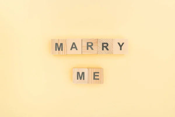 Vista superior de casarme letras hechas de bloques de madera sobre fondo amarillo - foto de stock