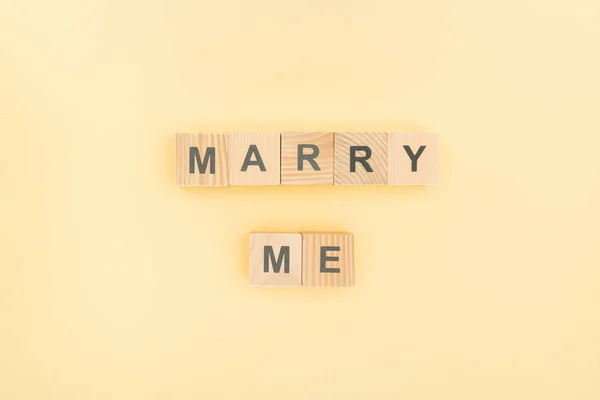 Top view of marry me lettering made of wooden blocks on yellow background — Stock Photo