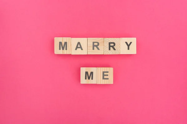 Top view of marry me lettering made of wooden cubes on pink background — Stock Photo