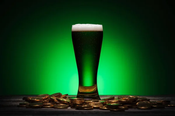 Vetro di birra verde vicino monete d'oro su sfondo verde — Foto stock