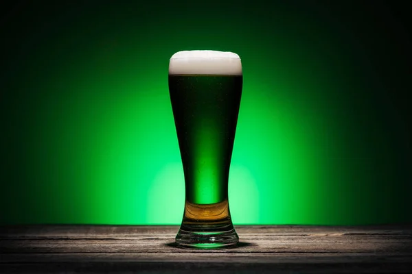 Vidro de cerveja em pé sobre mesa de madeira no dia st patricks no fundo verde — Fotografia de Stock