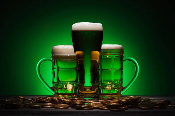 Glasses of beer standing near golden coins on st patricks day on green background — Stock Photo