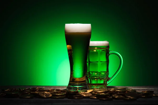 Verres de bière irlandaise debout près de pièces d'or sur table en bois sur fond vert — Photo de stock