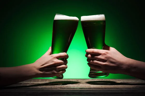 Vista recortada de los hombres tostadas con vasos de cerveza irlandesa en st patricks día sobre fondo verde - foto de stock