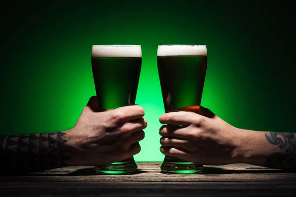 Vista cortada de homens segurando copos de cerveja irlandesa no fundo verde — Fotografia de Stock