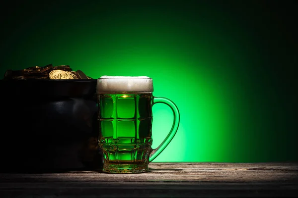 Vetro di birra vicino pentola con oro sulla st patricks giorno su sfondo verde — Foto stock