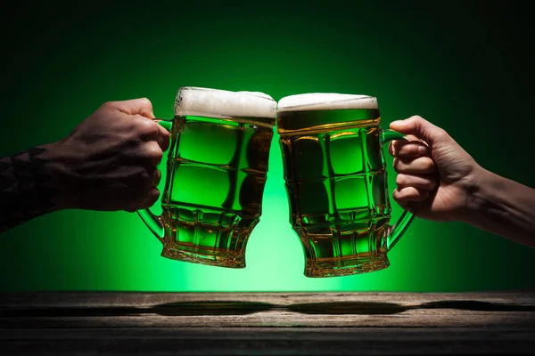 Vista recortada de amigos tostadas con vasos de cerveza en st patricks día sobre fondo verde - foto de stock