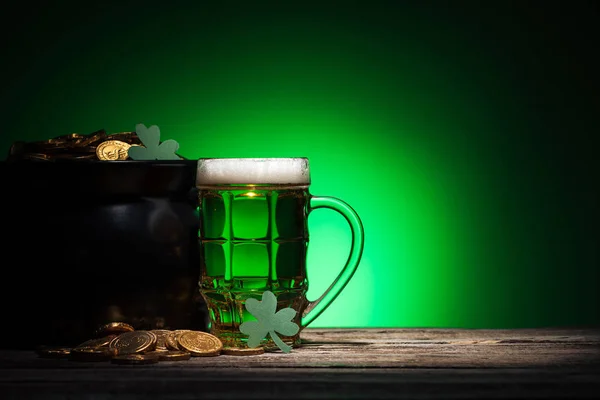 Vaso de cerveza cerca de olla con oro y tréboles en st patricks día sobre fondo verde - foto de stock