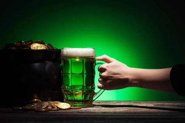 Vista recortada de hombre tostado vaso de cerveza irlandesa con olla de oro sobre fondo verde - foto de stock