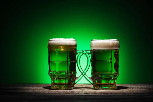 Bicchieri di birra irlandese in piedi su un tavolo di legno su sfondo verde — Foto stock